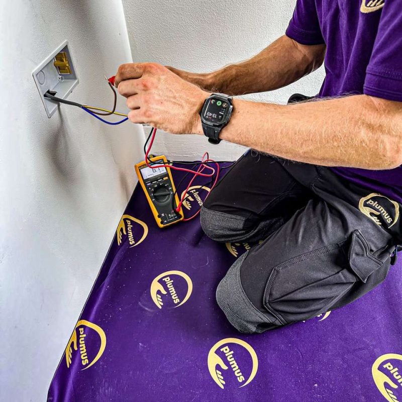 Plumus technician wires some electrics while kneeling on a Plumus branded mat